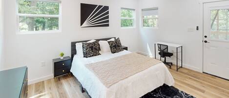 A modern bedroom with a bed, nightstands, a desk, and a ceiling fan.