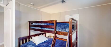 A room with a bunk bed, a door, a small bedside table, and a ceiling vent.
