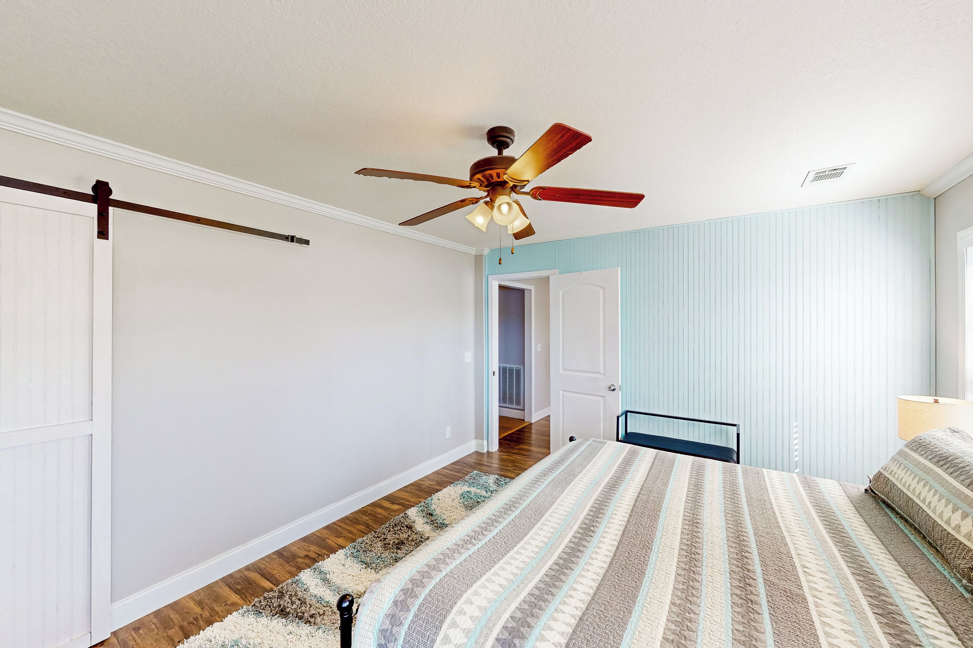 Une chambre à coucher avec un lit, un ventilateur de plafond, une porte et un couloir.