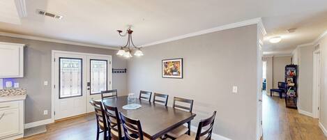 A dining area with a large wooden table, six chairs, and a chandelier.