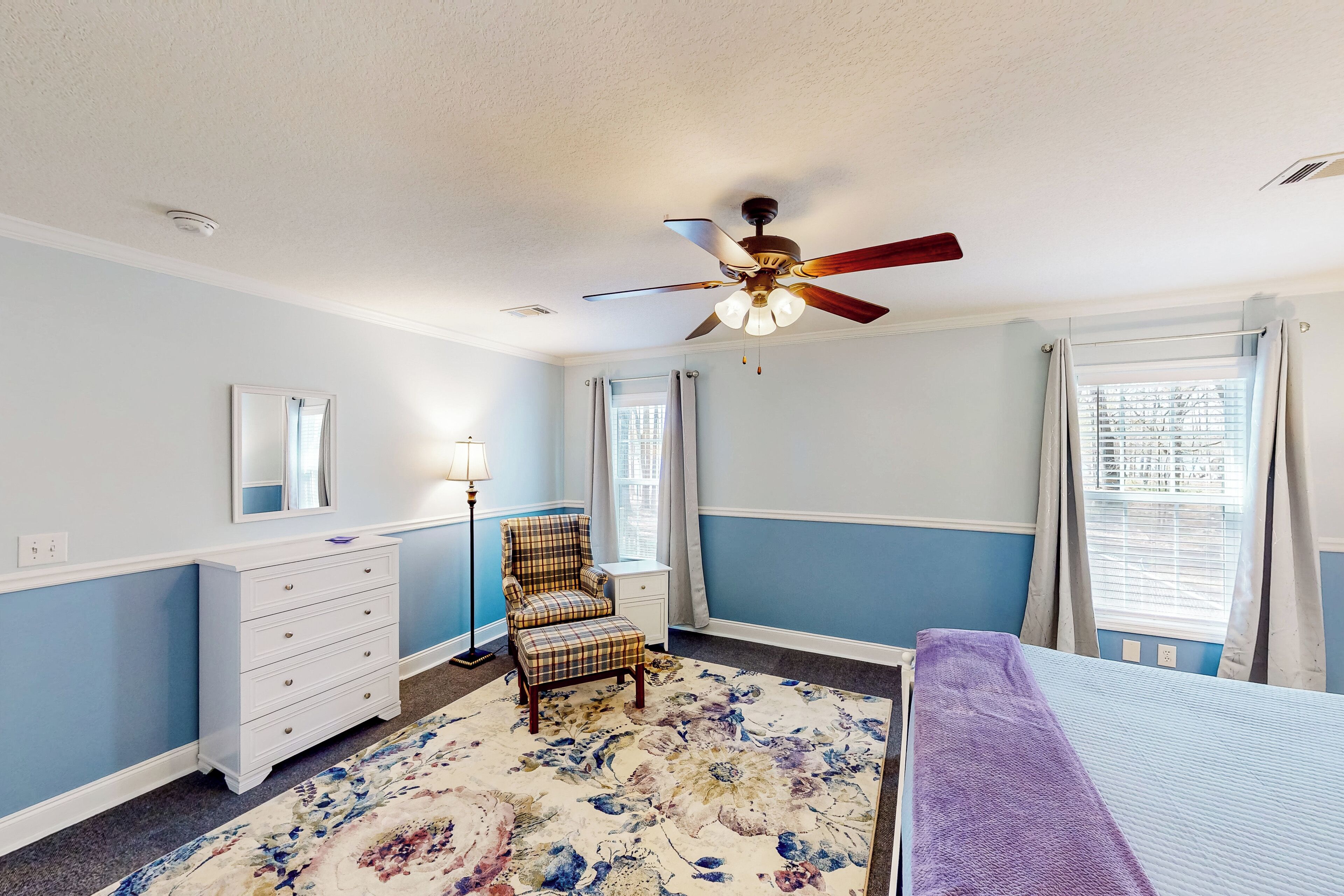 A bedroom with a bed, a dresser, a chair, a ceiling fan, and a window with curtains.