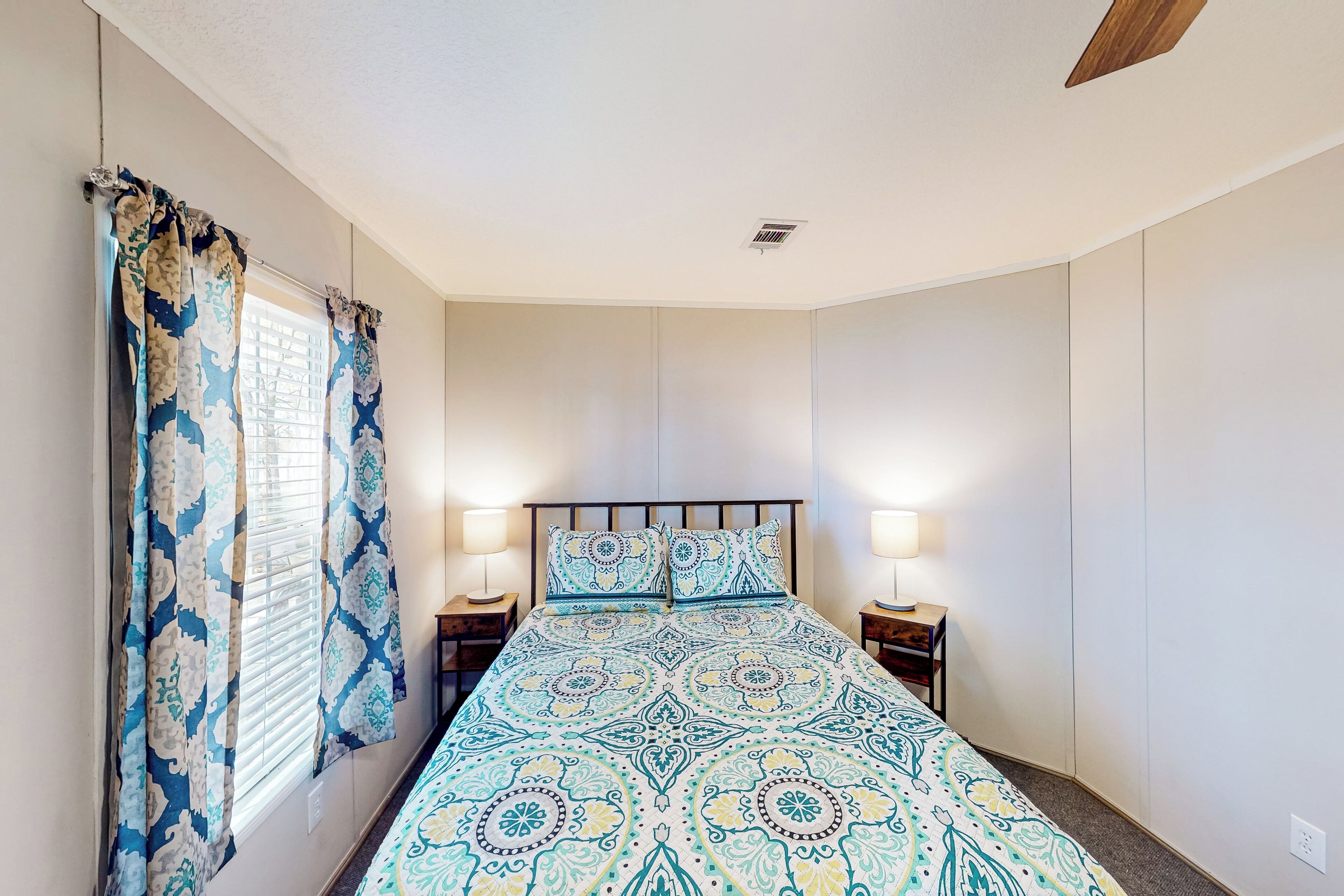 A bedroom with a bed, curtains, two bedside lamps, and a ceiling fan.