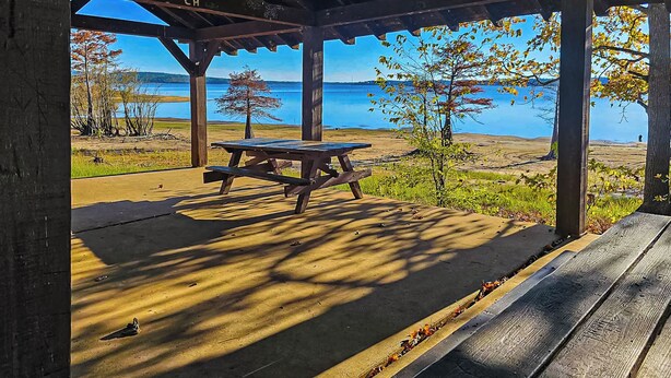A covered picnic area with a table and benches, overlooking a lake and grassy landscape. - 2BR Dog-friendly Home Near Lake w/ Fire Pit (San Augustine)