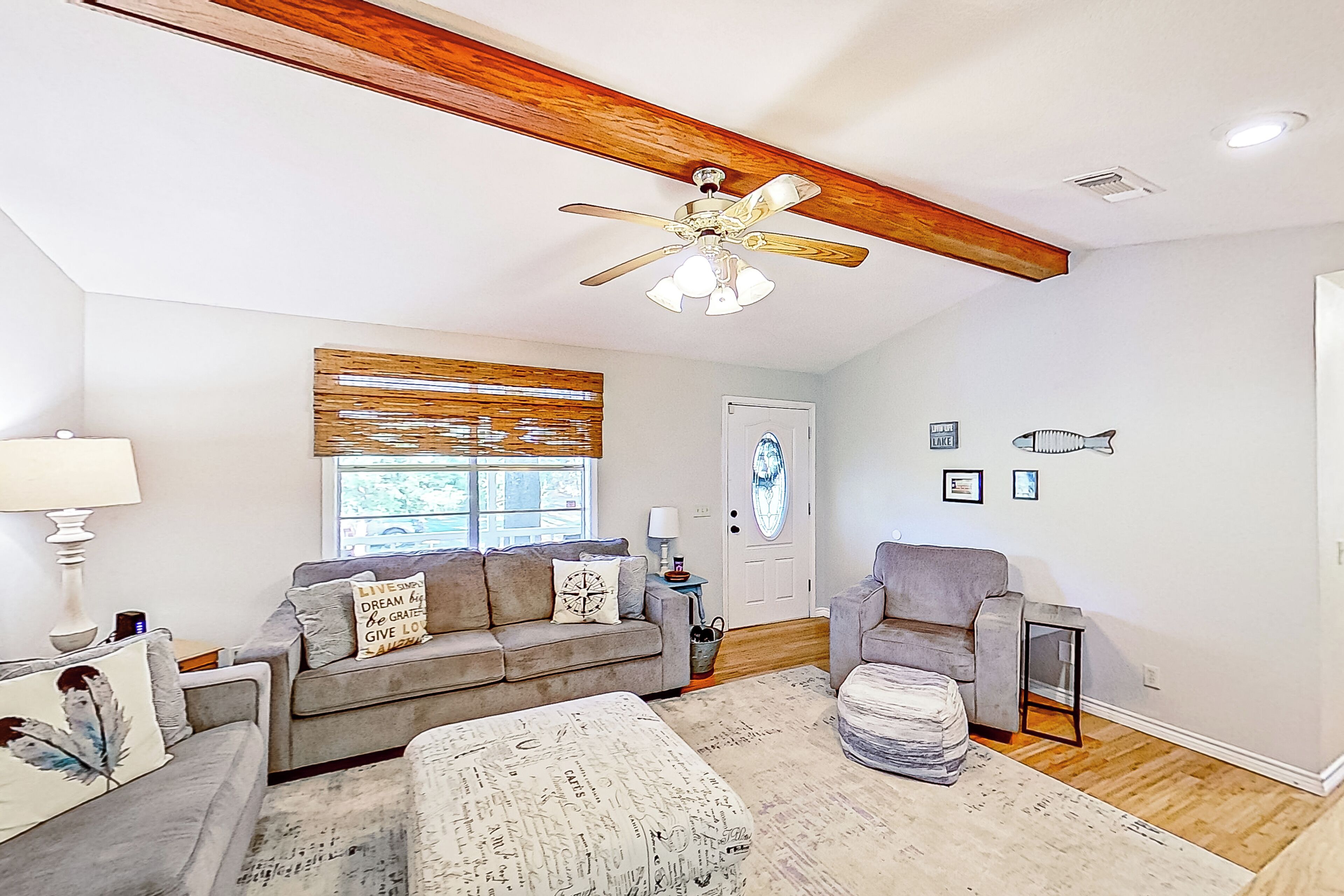 A spacious living room with a ceiling fan, a gray sofa, a coffee table, and a door with a decorative mirror.