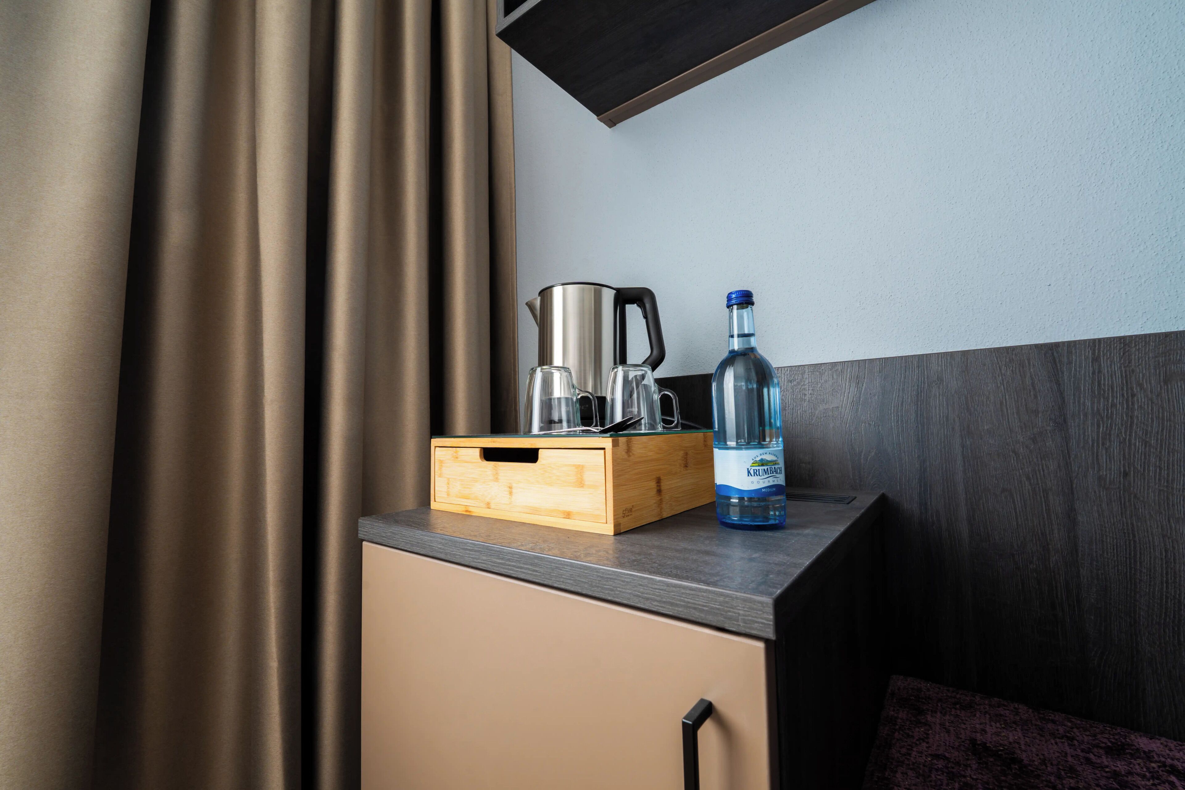 A kitchenette with a coffee maker, a bottle of water, and a wooden box containing glasses and a kettle.