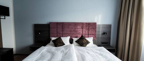 A hotel room with a large bed, a headboard, two bedside tables, and a TV on the wall.