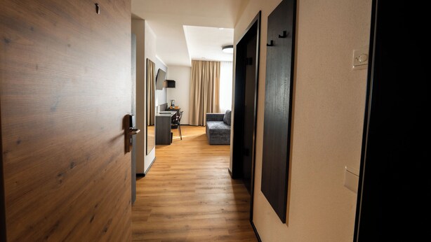 Un couloir avec un plancher en bois, un canapé, une petite table et un miroir au mur.