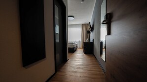 Un couloir étroit, doté d’un plancher en bois, mène à une chambre à coucher qui contient un lit et une fenêtre.
