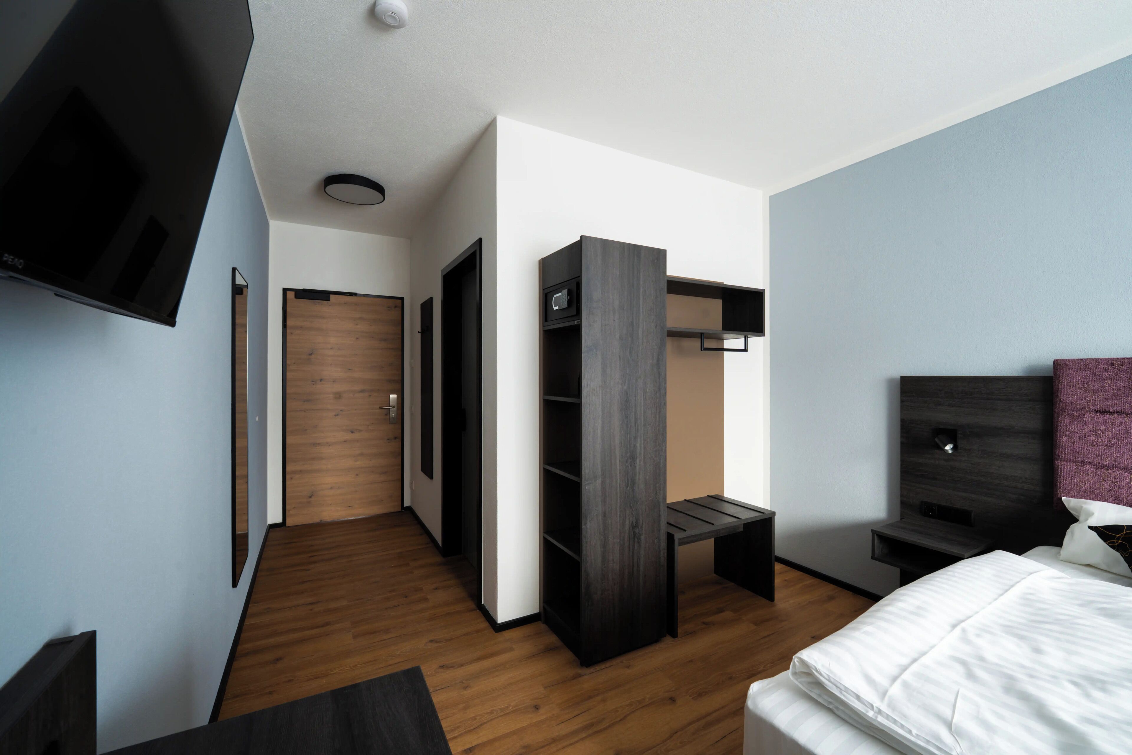Una habitación de hotel moderna con suelo de madera, una cama, un televisor, un armario y un escritorio.