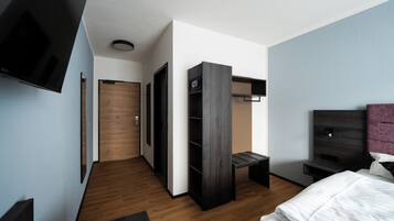 Una habitación de hotel moderna con suelo de madera, una cama, un televisor, un armario y un escritorio.