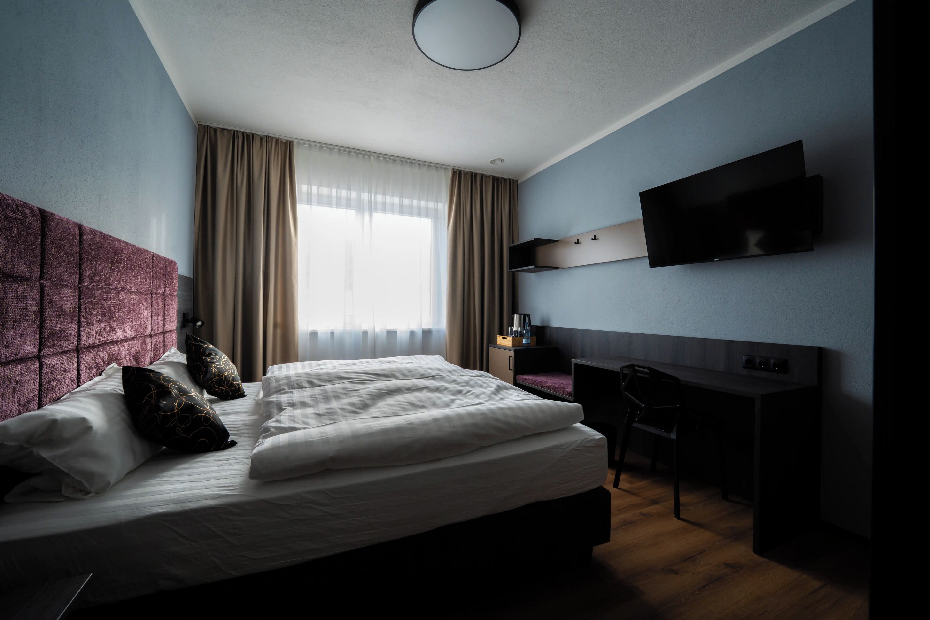 Une chambre d’hôtel moderne, dotée d’un grand lit, d’un bureau et d’un téléviseur fixé au mur.