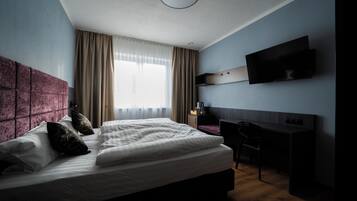 Une chambre d’hôtel moderne, dotée d’un grand lit, d’un bureau et d’un téléviseur fixé au mur.