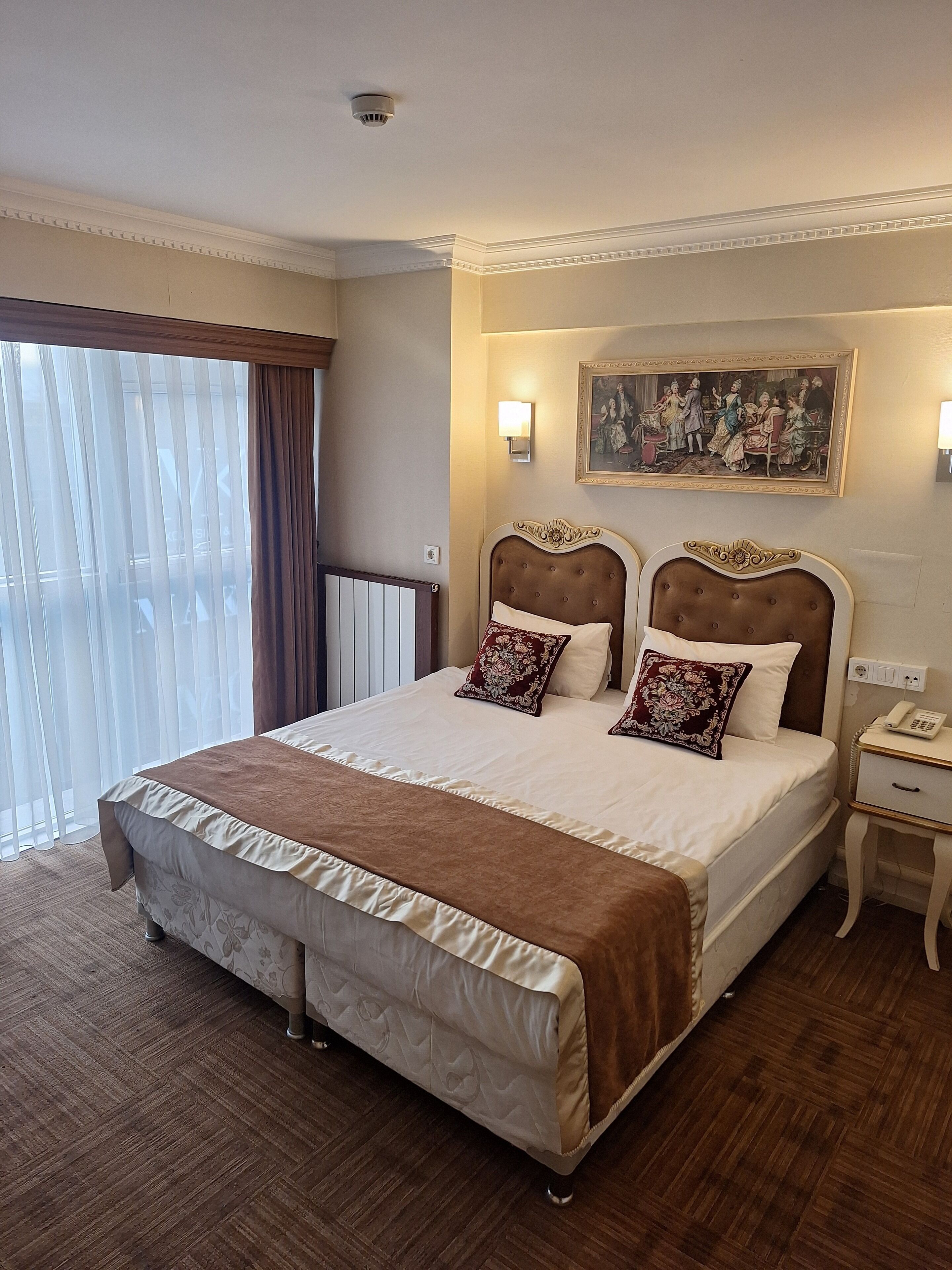 A large bed with a brown headboard, two pillows, and a bedside table with a phone.