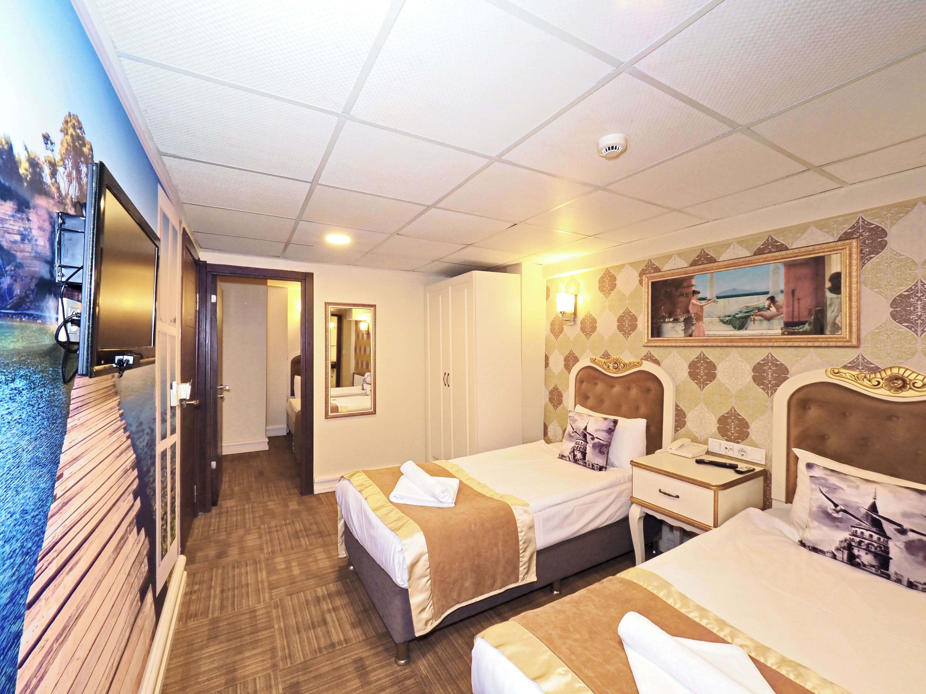 A hotel room with two beds, a television, a mirror, a painting, and a ceiling light.