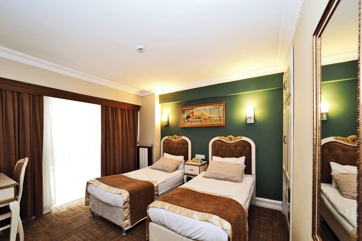 A hotel room with two beds, a desk, a chair, a painting on the wall, and a large mirror.