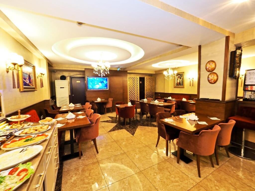 A restaurant with multiple dining tables and chairs, a buffet area with various dishes, and a television screen on the wall.