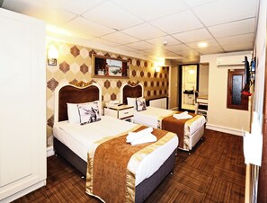 Une chambre d’hôtel avec deux lits, un bureau, un miroir et une salle de bain visible à travers une porte ouverte.