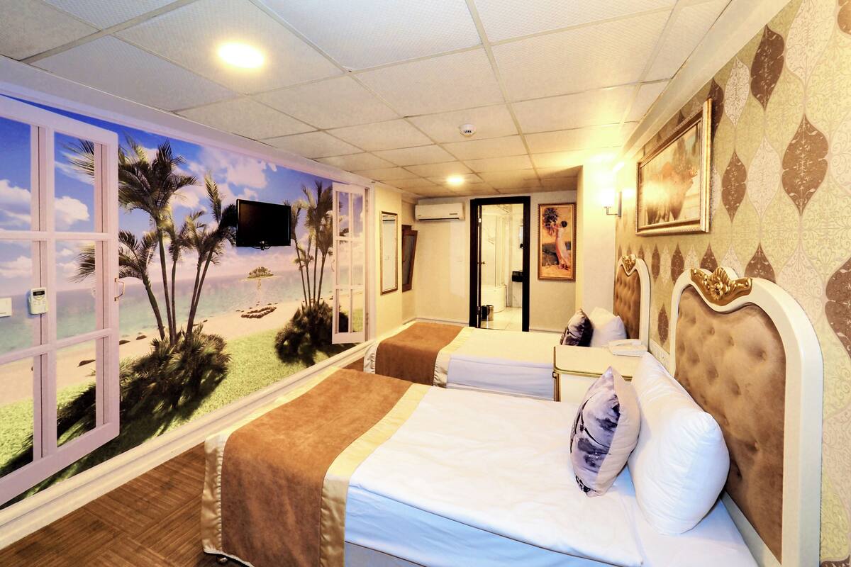 A hotel room with a beach mural, a bed, a bedside table, a TV, and a bathroom door.