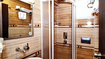 Un baño con tocador de madera, lavamanos, espejo, cabina de ducha e inodoro.