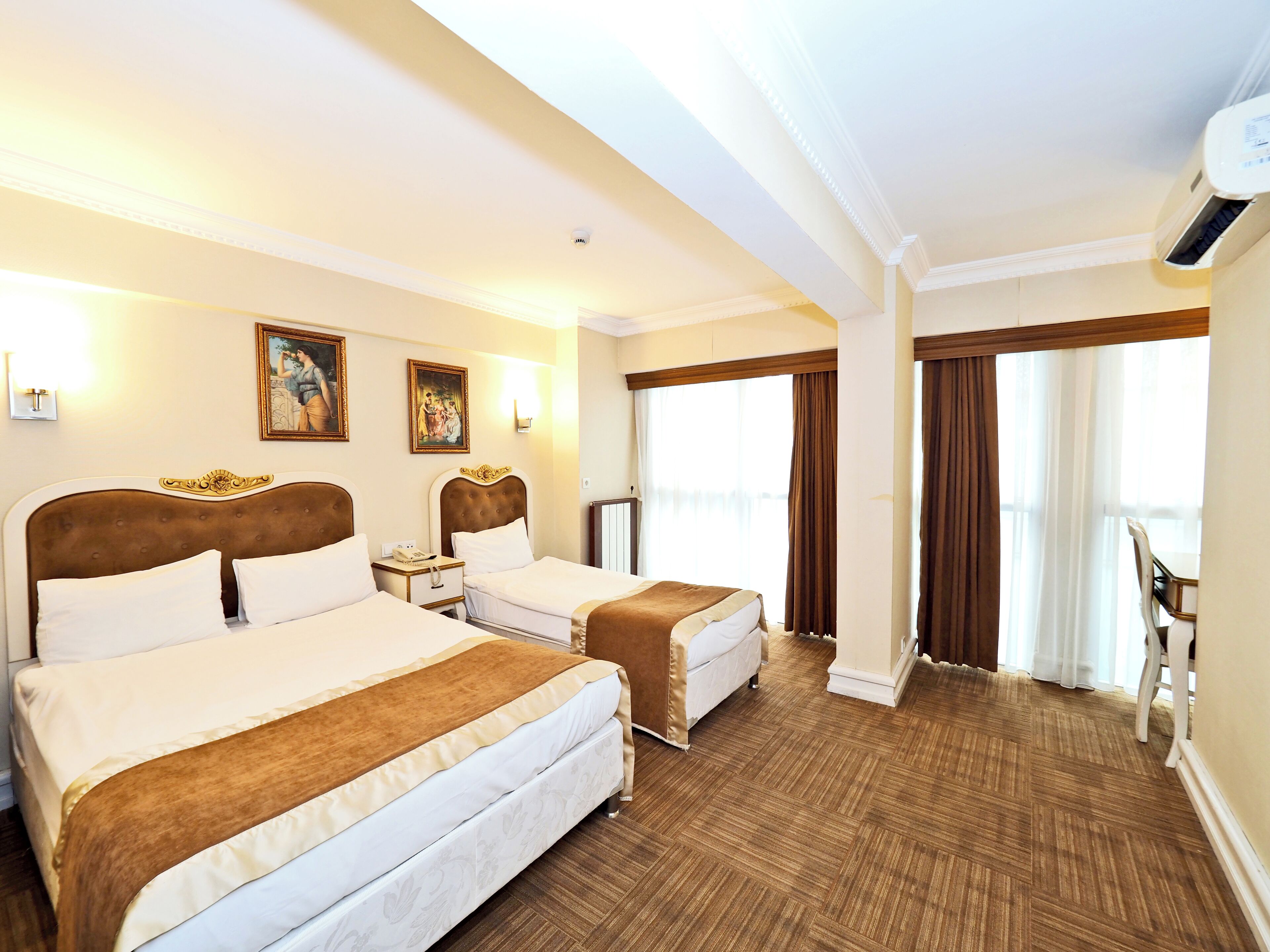 A hotel room with two beds, a desk, a chair, and a large window with curtains.