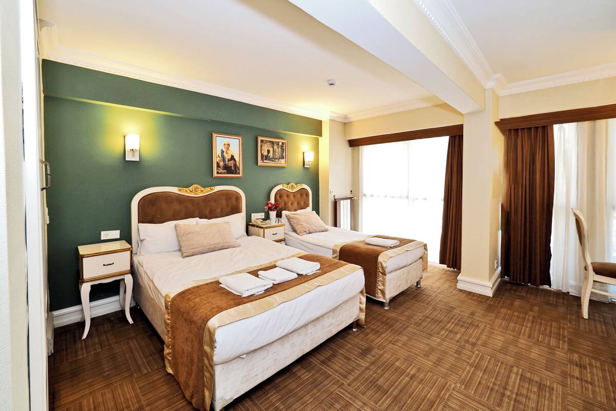A hotel room with two beds, a large window with curtains, a wooden floor, and artwork on the walls.
