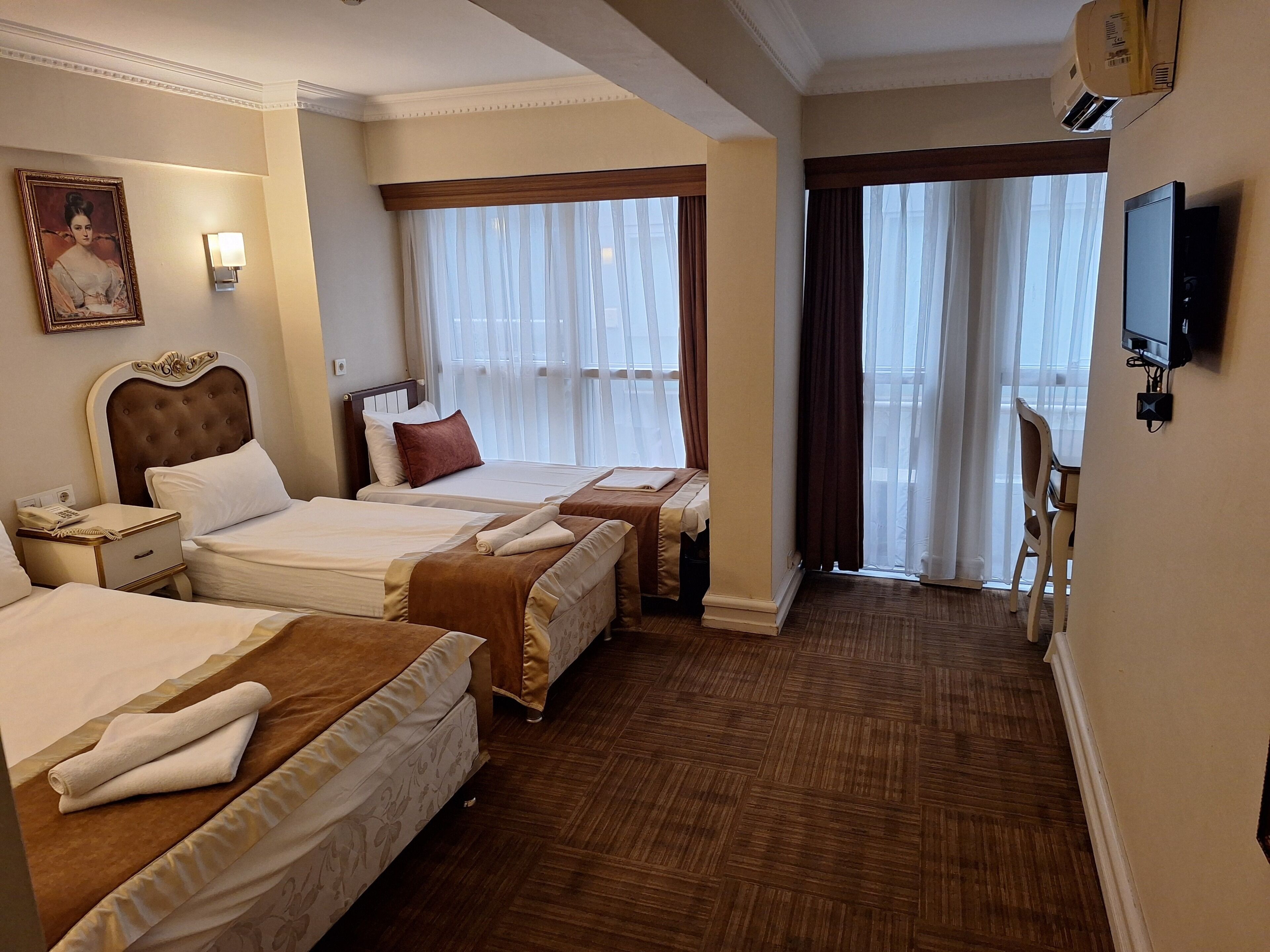 Habitación de hotel con dos camas, una mesita de noche con lámpara, un cuadro en la pared y un televisor también en la pared.