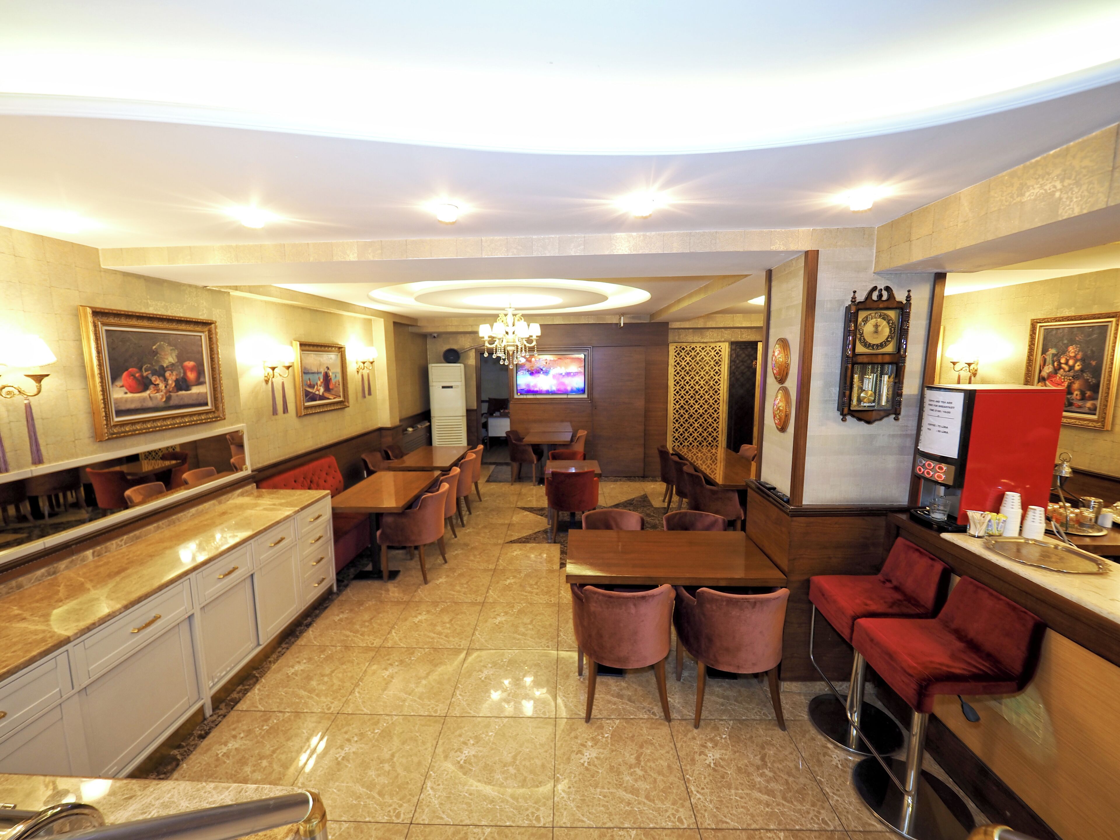 A hotel lobby with marble flooring, wooden tables and chairs, a bar area, and a chandelier.