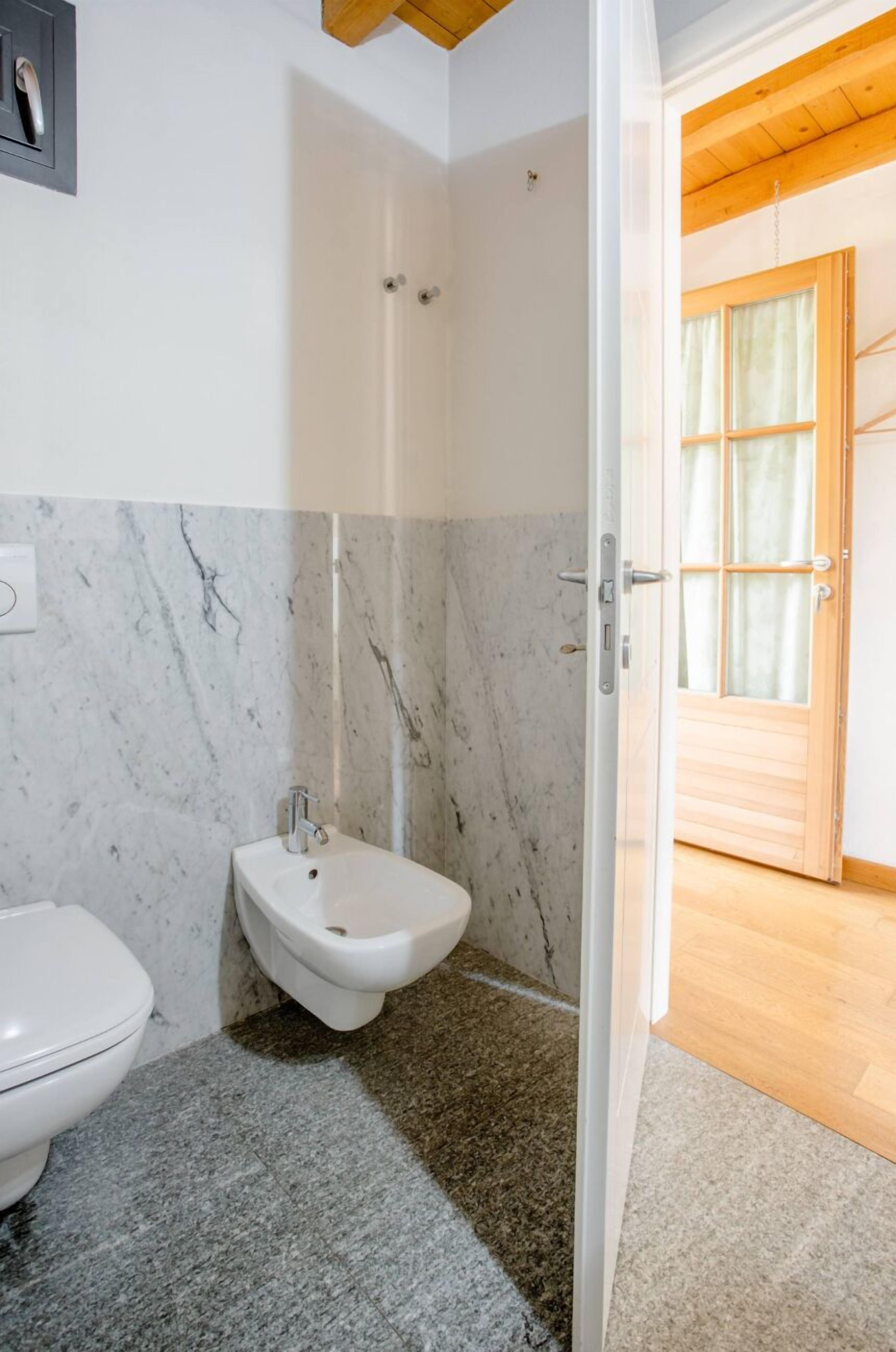 A bathroom with a marble wall, a white sink, and a toilet.