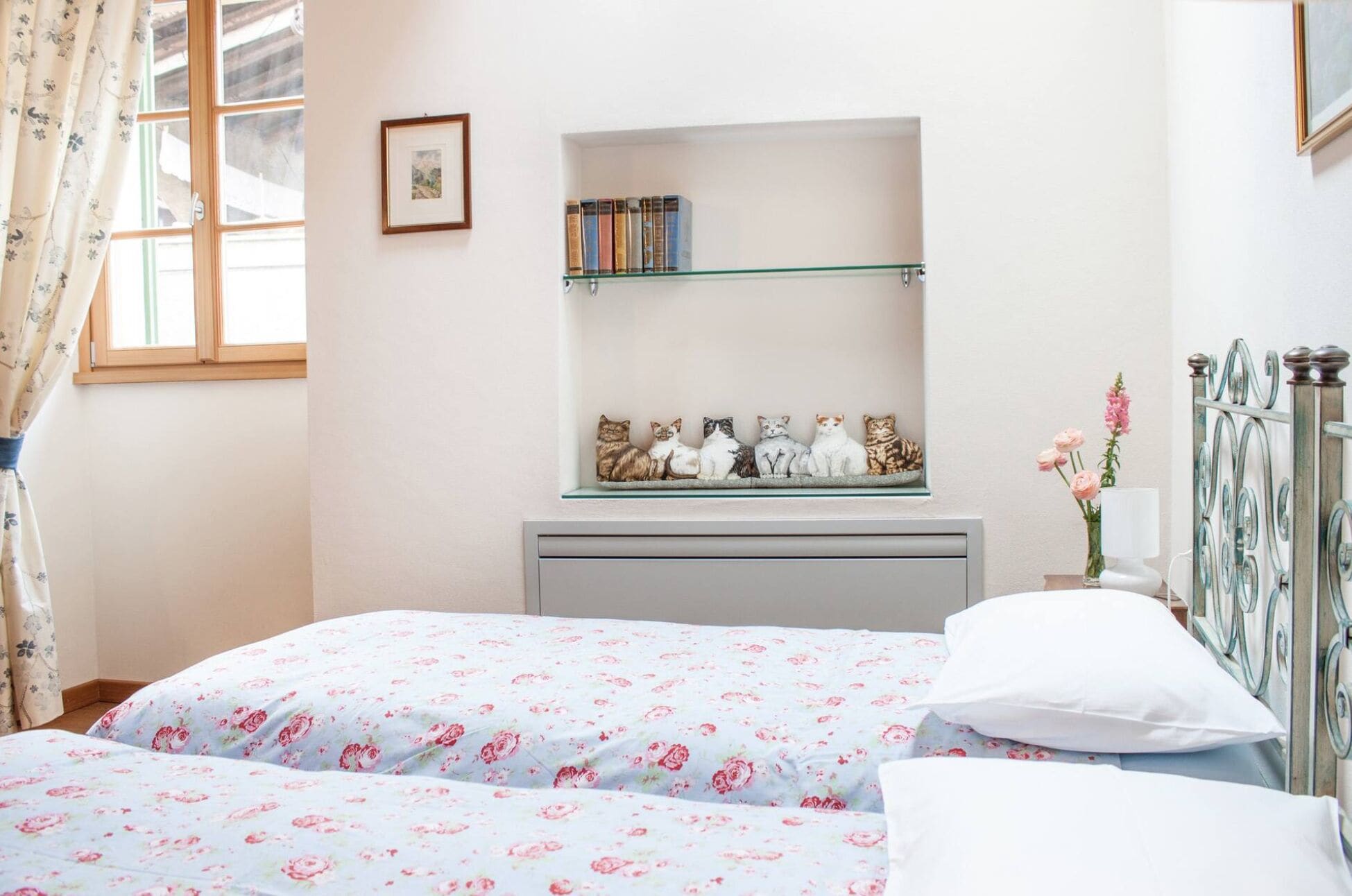 A bedroom with two beds, a bookshelf, and a window with curtains.