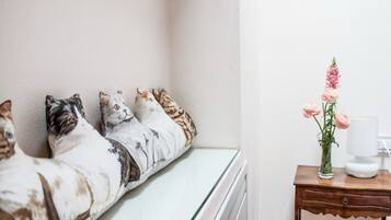 A bedroom with a bed against a wall, a bedside table with a vase of flowers, and a lamp.