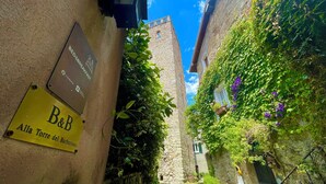 A narrow alleyway with a sign for 'B&B Alla Torre del Barbaressa' and a stone building with greenery and flowers. - Alla torre del barbarossa B&B Foresteria (Maggiana)