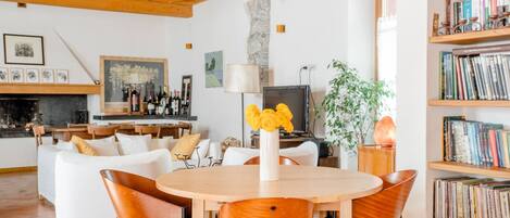 Una sala de estar acogedora con chimenea, un comedor con una mesa redonda y una estantería llena de libros.