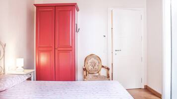 Quarto com cama, guarda-roupa vermelho, porta branca e uma cadeira.