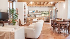 A spacious living room with a white sofa, a TV, and a dining area with wooden chairs and a table. - Alla torre del barbarossa B&B Foresteria (Maggiana)