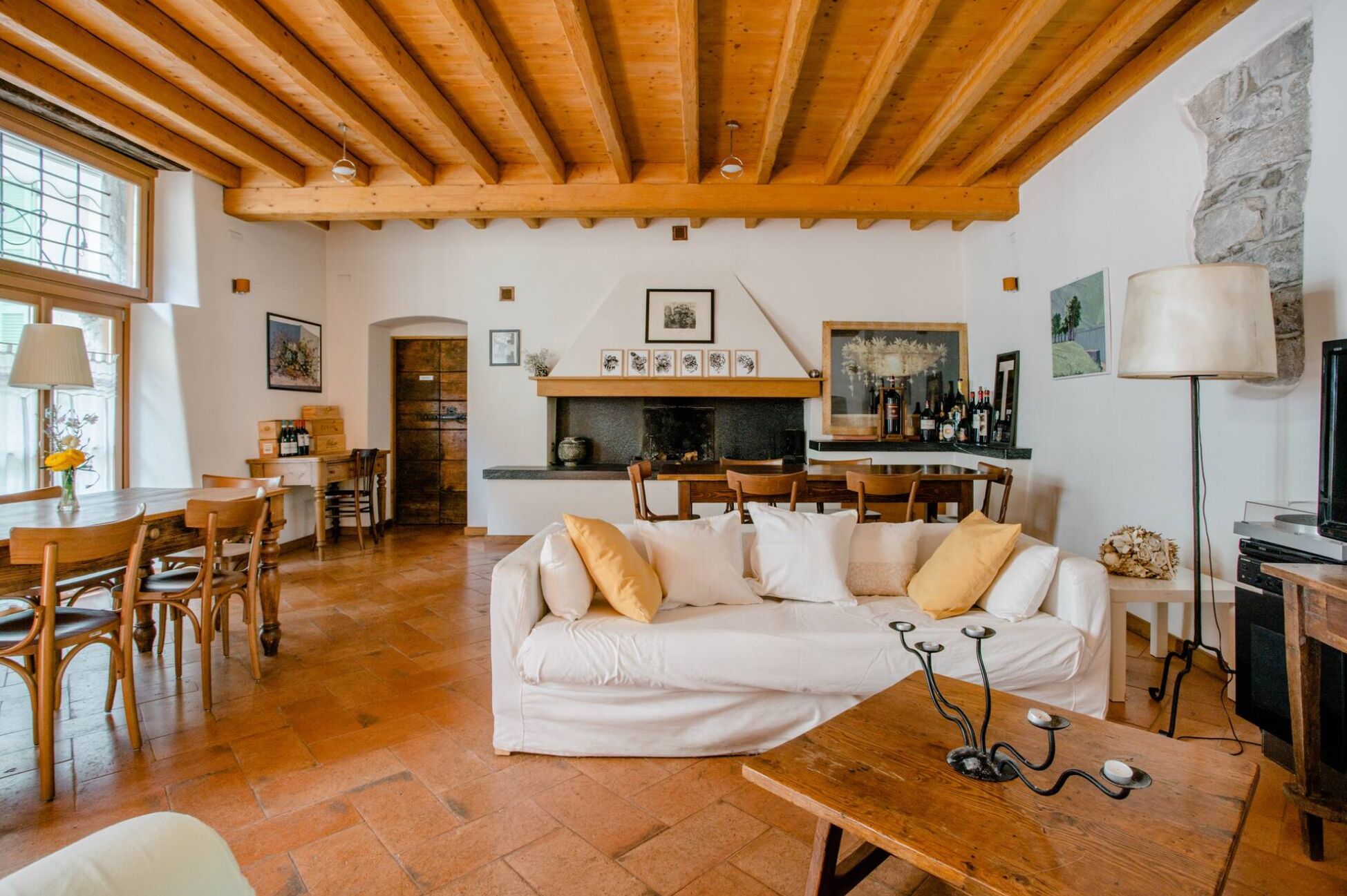 Una sala de estar acogedora con techo de madera, un sofá blanco y una zona de comedor con sillas de madera.