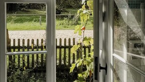 Huone, jossa on suuri ikkuna, puinen aita ja näkymä puutarhaan.