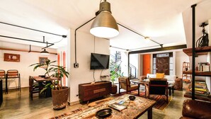 A spacious living area with a rustic wooden coffee table, a comfortable sofa, and a dining table with chairs. There is a large plant in a pot, a television mounted on the wall, and a bookshelf filled with books. - w Bright Colonial 5BR House With Balcony (Medellín)
