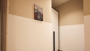 Un couloir aux murs peints dans des tons de beige et de blanc, doté d’un plancher en bois et orné d’un tableau représentant un pont.
