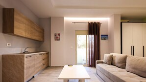 A modern living room with a sofa, a dining table, and a kitchen area with wooden cabinets. - Azzurra Studio 02 in Durr s (Durrës)