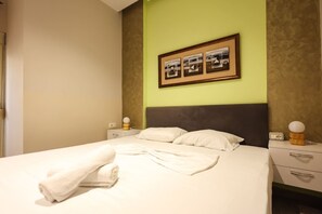 A neatly made bed with a white comforter and pillows, a framed photo above the headboard, and a bedside table with a lamp. - Azzurra Studio 01 in Durr s (Durrës)