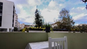 A balcony with a white chair and a table, overlooking a cityscape with buildings and trees. - Azzurra Studio 03 in Durr s (Durrës)