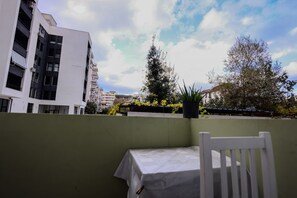A balcony with a white table and chair, overlooking a cityscape with modern buildings and a tree. - Azzurra Studio 03 in Durr s (Durrës)