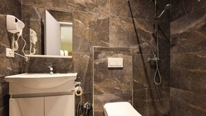A modern bathroom with a marble wall, a white sink, a toilet, a shower, and a hairdryer mounted on the wall. - Azzurra Studio 03 in Durr s (Durrës)
