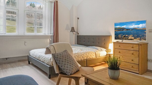 A bedroom with a bed, a chair, a dresser, a lamp, a window, and a painting. - Apartment at the Saxon Switzerland National Park (Sebnitz)