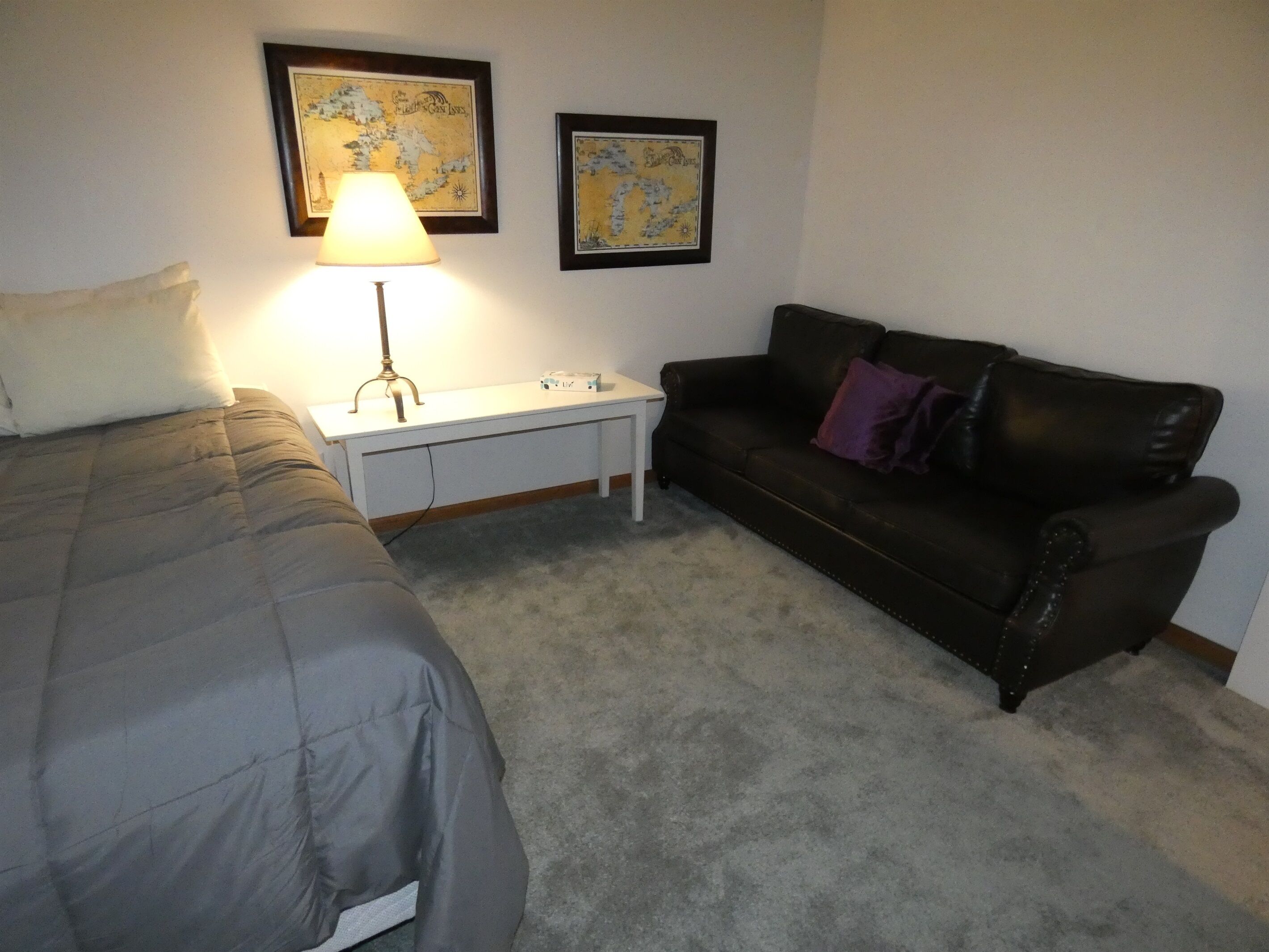 A bedroom with a bed, a desk, a couch, and two framed maps on the wall.