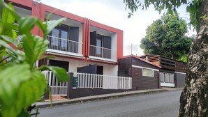 Un edificio residencial moderno de dos pisos con balcones, una entrada con portón y un árbol en primer plano.