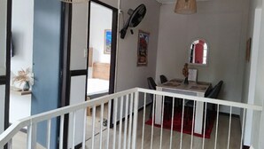 Un comedor con una mesa blanca, sillas y un tapete rojo. Se observa una barandilla blanca en primer plano.