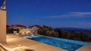 Une piscine avec des chaises longues et une vue sur la mer au crépuscule.