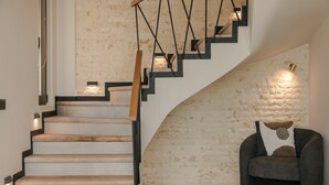 Un escalier avec des marches en bois et des rampes en métal noir, menant à un palier doté d’un mur en pierre et d’un fauteuil rembourré agrémenté d’un coussin décoratif.
