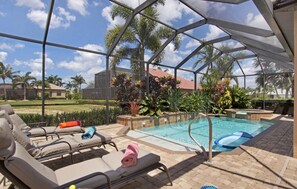 A covered outdoor swimming pool with lounge chairs and a view of palm trees and a house in the background. - Experience the Florida dream at Villa Barbara in Cape Coral! (Cape Coral)